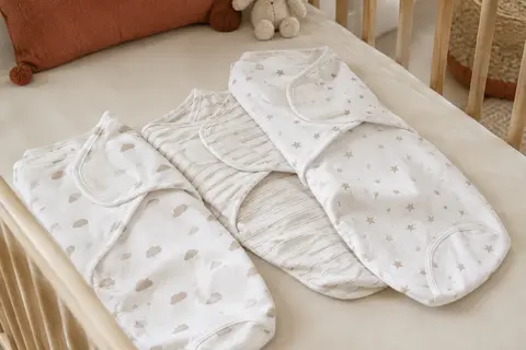 Trois langes blancs d’emmaillotage en coton biologique, avec fermeture Velcro et motifs de nuages, rayures et étoiles.